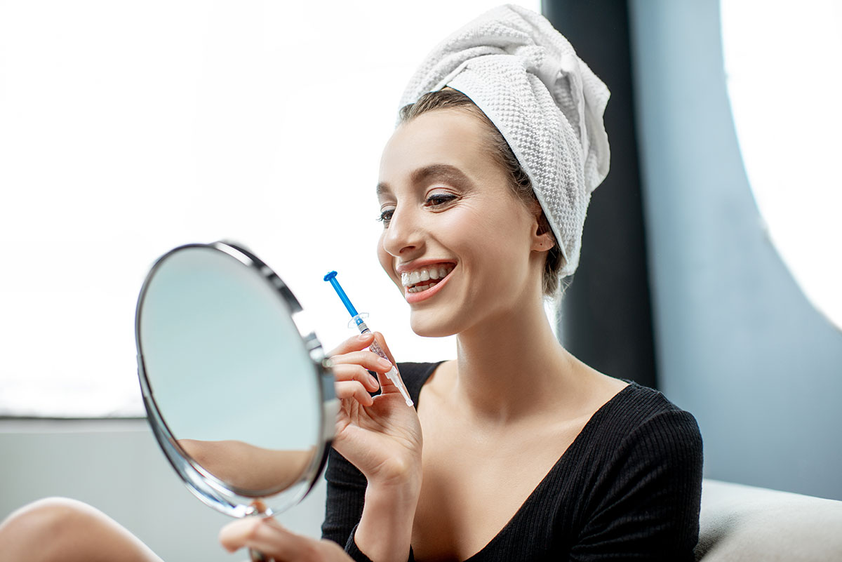 at-home teeth whitening kits woman smiling in mirror after using at-home teeth whitening kits
