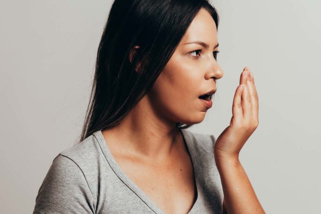 causes-of-bad-breath woman checking to see what could be the cause of bad breath
